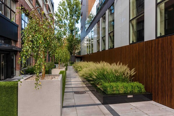 A modern building with large windows, a concrete pathway, and various plants.
