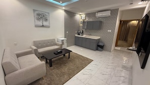 A modern living room with a sofa, coffee table, and a painting of a tree. - Qimam Park Hotel 3 Abha (Abha)