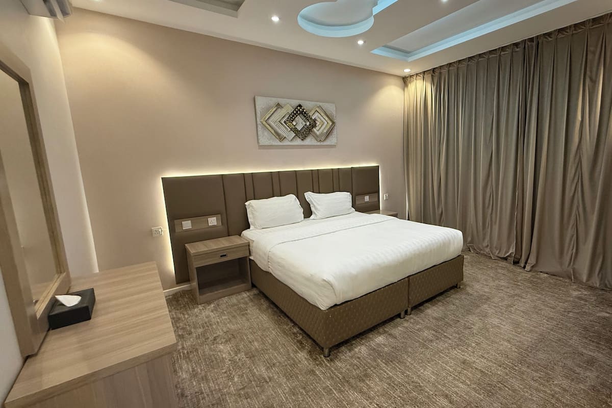 Une chambre d’hôtel moderne, dotée d’un grand lit, d’une table de chevet, d’un luminaire fixé au mur et d’un élément décoratif mural.