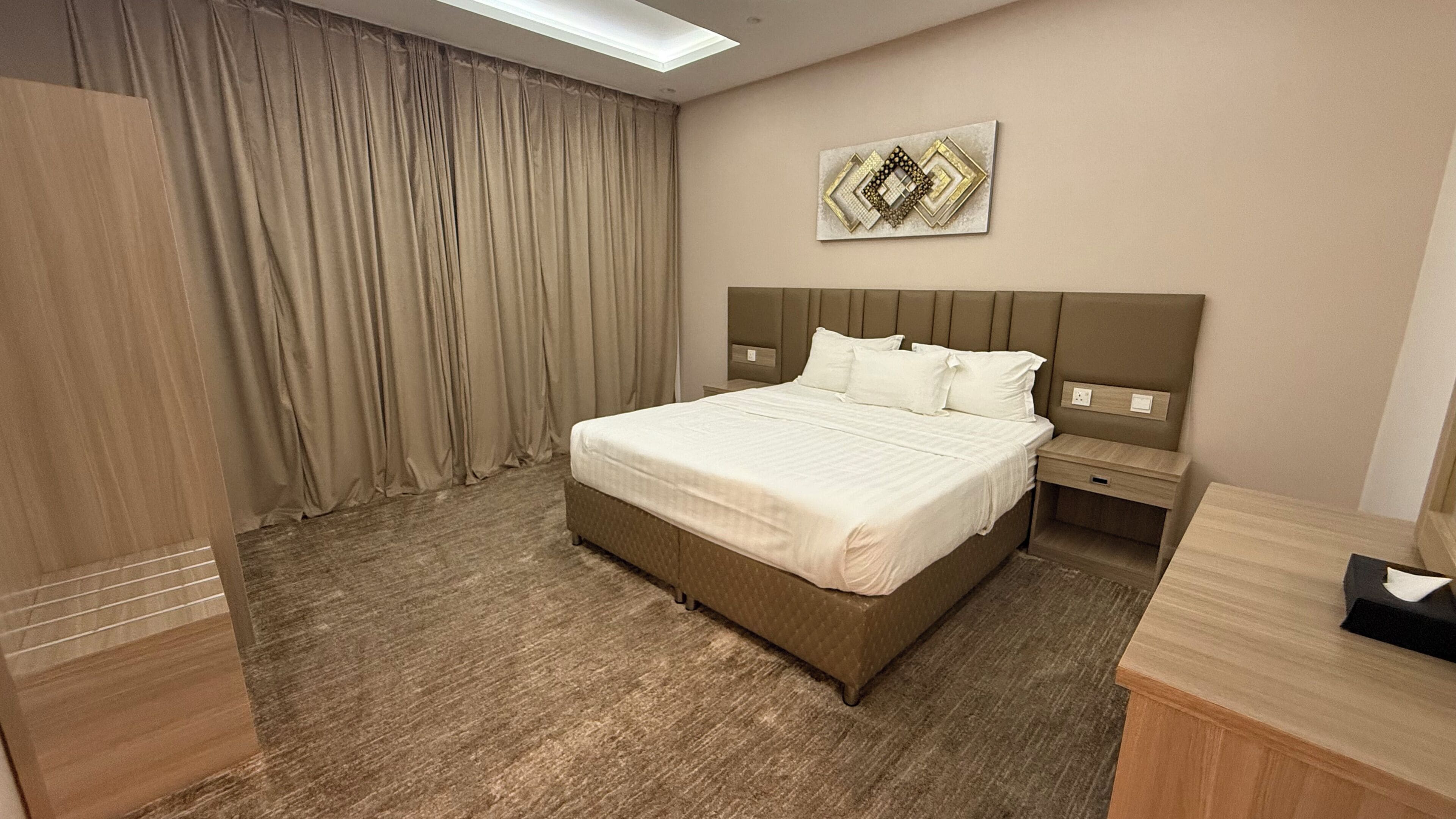 A hotel room with a large bed, a nightstand, a desk, and a wall-mounted artwork.