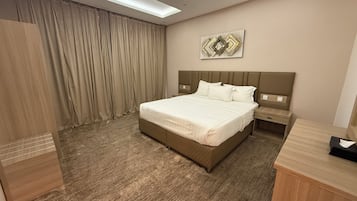 A hotel room with a large bed, a nightstand, a desk, and a wall-mounted artwork.