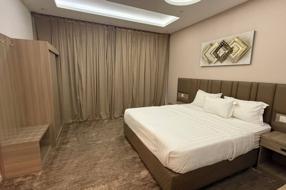 Une chambre d’hôtel avec un grand lit, une table de chevet, une armoire et un luminaire au plafond.