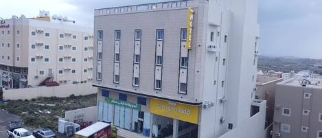 A hotel with a modern design, featuring a prominent yellow sign, multiple windows, and a parking area with a few vehicles.
