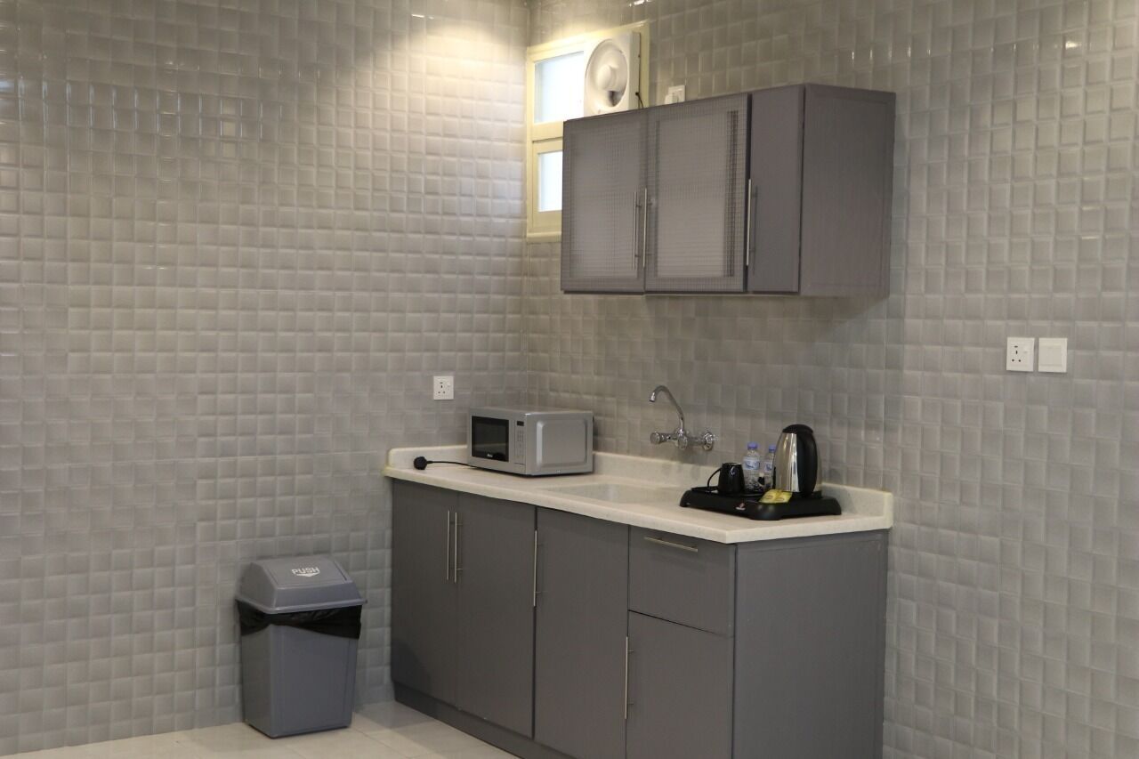 Una cocina compacta con armarios grises, un microondas, una tetera y un cubo de basura.