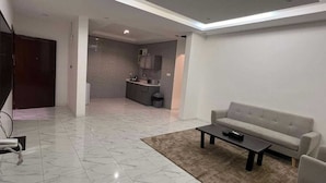 A modern living room with a sofa, a coffee table, and a kitchen area in the background. - Qimam Park Hotel 3 Abha (Abha)
