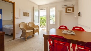 A room with a dining table, red chairs, wicker chairs, a bed, and a view of greenery outside. - Casa Bellaria | RivedelSalento - Casa Bellaria piano terra (Castro)