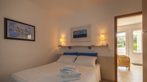 A bedroom with a bed, a framed painting, two wall-mounted lamps, and a view of the outdoors. - Casa Bellaria | RivedelSalento - Casa Bellaria piano terra (Castro)