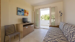 A living room with a sofa, a TV on a wooden cabinet, a chair, and a balcony with a view of trees. - Casa Bellaria primo piano (Castro)