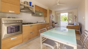 A modern kitchen with wooden cabinets, a gas stove, and a built-in oven. There is a dining area with a glass table and chairs. - Casa Bellaria primo piano (Castro)