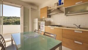A modern kitchen with a glass dining table, wooden cabinets, a built-in oven, and a gas stove. - Casa Bellaria primo piano (Castro)