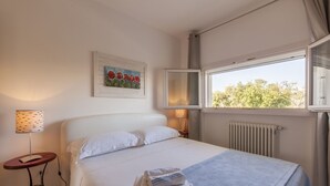 A bedroom with a bed, a window with a view, a radiator, a lamp, and a painting on the wall. - Casa Bellaria primo piano (Castro)