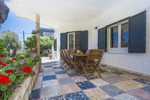 Un patio con piso de baldosas, una mesa de madera con sillas y una ventana con contraventanas.