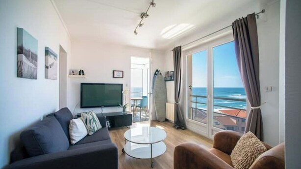 A modern living room with a flat-screen TV, a sofa, a coffee table, and a view of the ocean through large windows. - Apartment by the sea with exceptional views (Soorts-Hossegor)