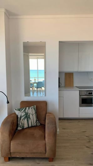 A modern living room with a brown sofa and a view of the beach through a large window.