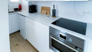 A modern kitchen with white cabinetry, a black stovetop, and a built-in oven. - Apartment by the sea with exceptional views (Soorts-Hossegor)