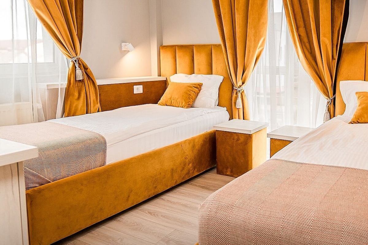 A hotel room with two beds, a small table, and a window with curtains.