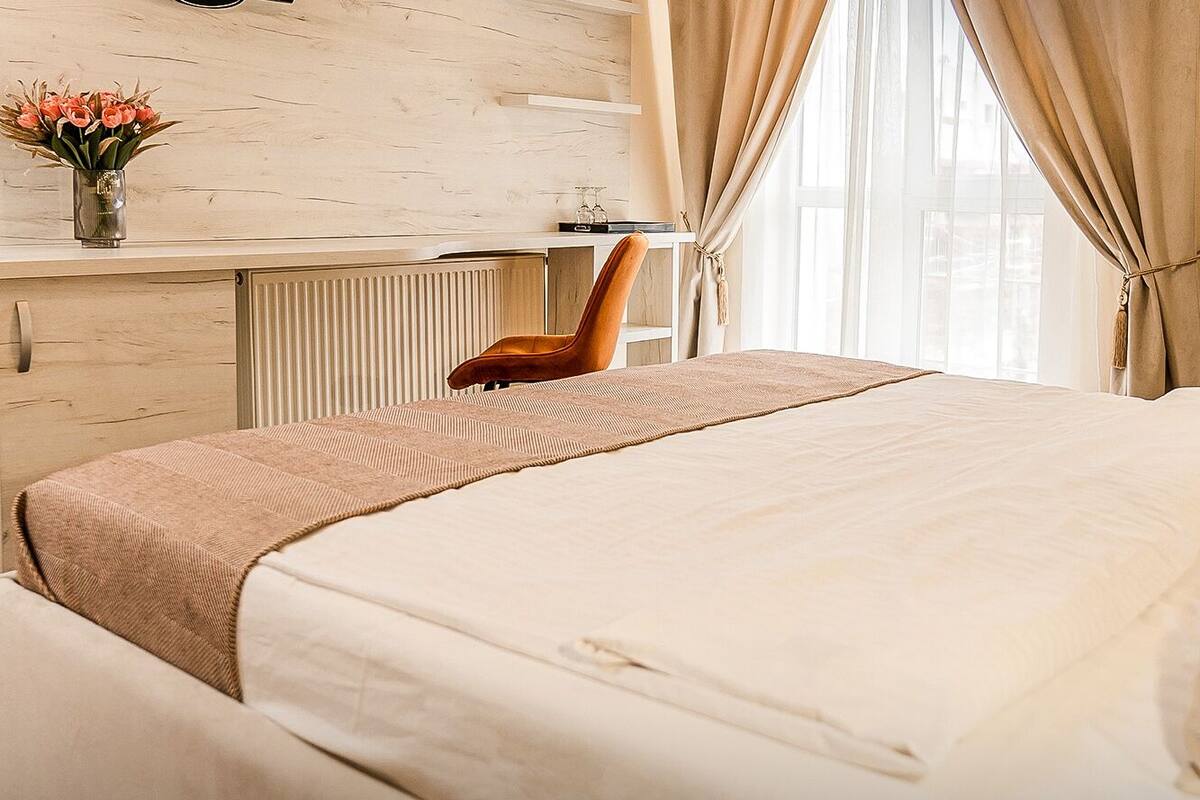 Une chambre d’hôtel avec un lit, une chaise, un bureau agrémenté d’un vase de fleurs et une fenêtre avec des rideaux.