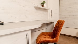 A modern room with a white marble wall, a white desk with drawers, a small potted plant, and a single orange chair. - PENSIUNEA ELISEI (Timisoara)