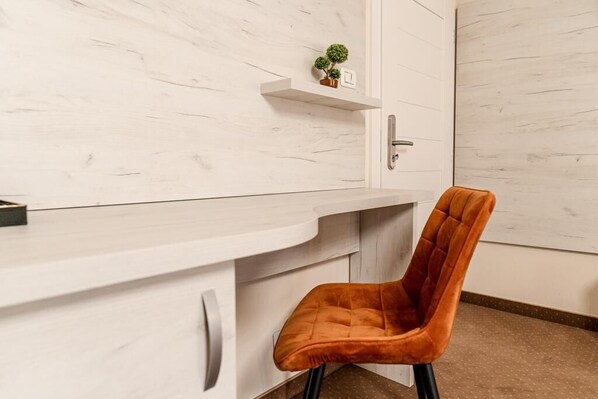 A modern room with a white marble wall, a white desk with drawers, a small potted plant, and a single orange chair.