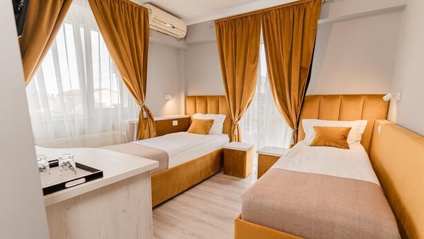 A hotel room with two beds, a small desk, and a window with curtains. - PENSIUNEA ELISEI (Timisoara)