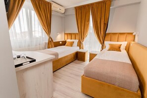 A hotel room with two beds, a small desk, and a window with curtains.