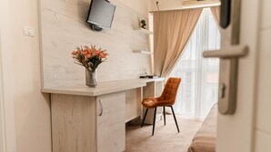 A small, modern room with a wooden desk, a chair, a TV mounted on the wall, and a window with curtains. - PENSIUNEA ELISEI (Timisoara)