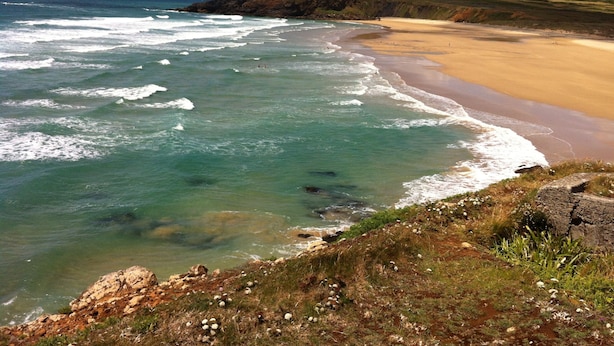 A coastal landscape with a sandy beach and rocky cliffs.