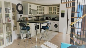 A compact kitchen with a central island, a washing machine, and a dining area with chairs.