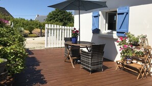 A wooden deck with a table and chairs, a potted plant, and a blue umbrella.