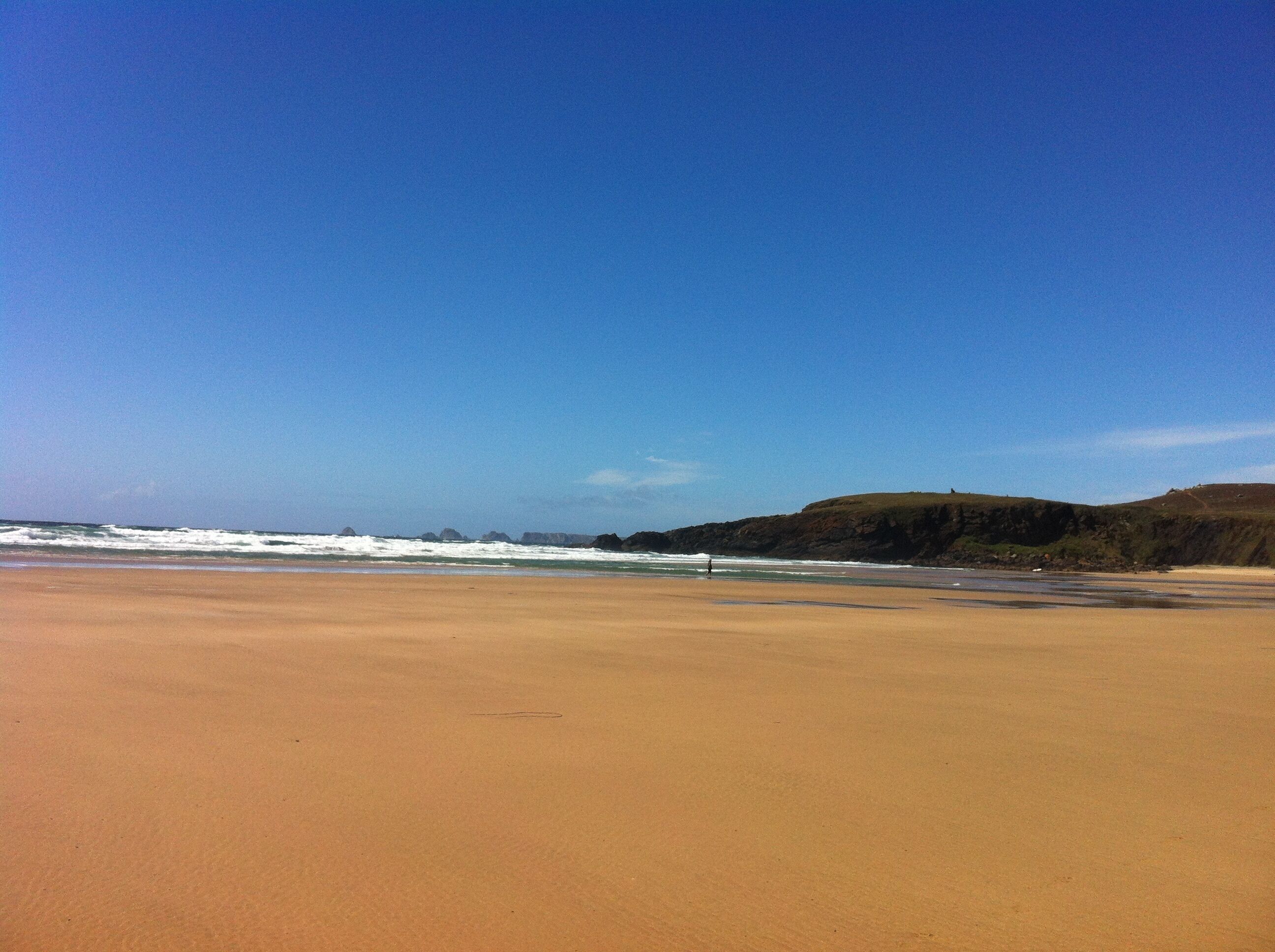 A wide sandy beach with gentle waves and a clear blue sky.