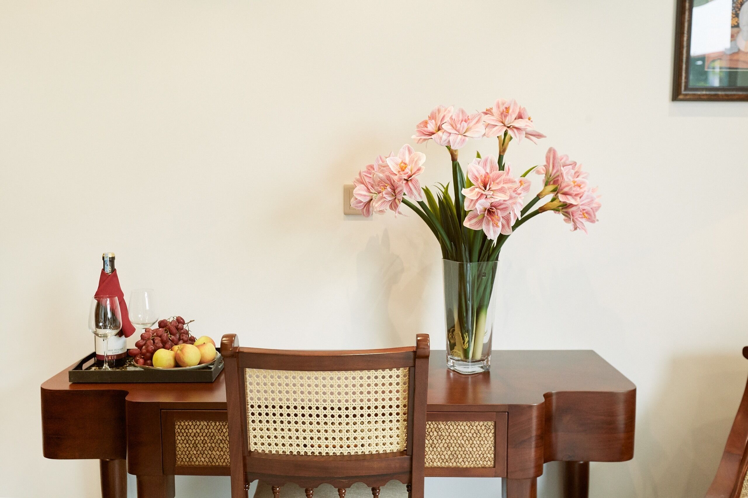 A wooden table with a tray of fruits, a bottle of wine, and a vase of flowers.