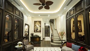 A spacious lobby with a high ceiling fan, a staircase, and a seating area with a patterned rug. - Camellia Residence Hanoi (Hanoi)