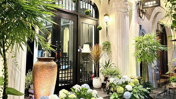 A hotel entrance with a black sign, large potted plants, and hanging greenery. - Camellia Residence Hanoi (Hanoi)