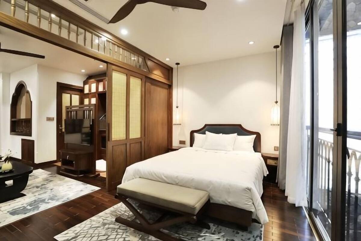 A hotel room with a large bed, a bench, a television, and a balcony with curtains.