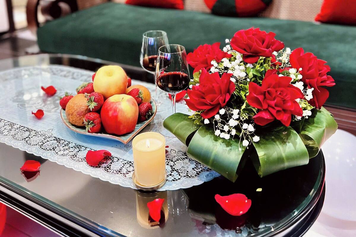 A dining table with fruits, wine glasses, a candle, and a bouquet of flowers.