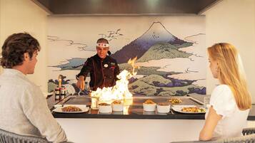 Un restaurante con un chef realizando una técnica culinaria a base de fuego, sirviendo comida a los comensales.
