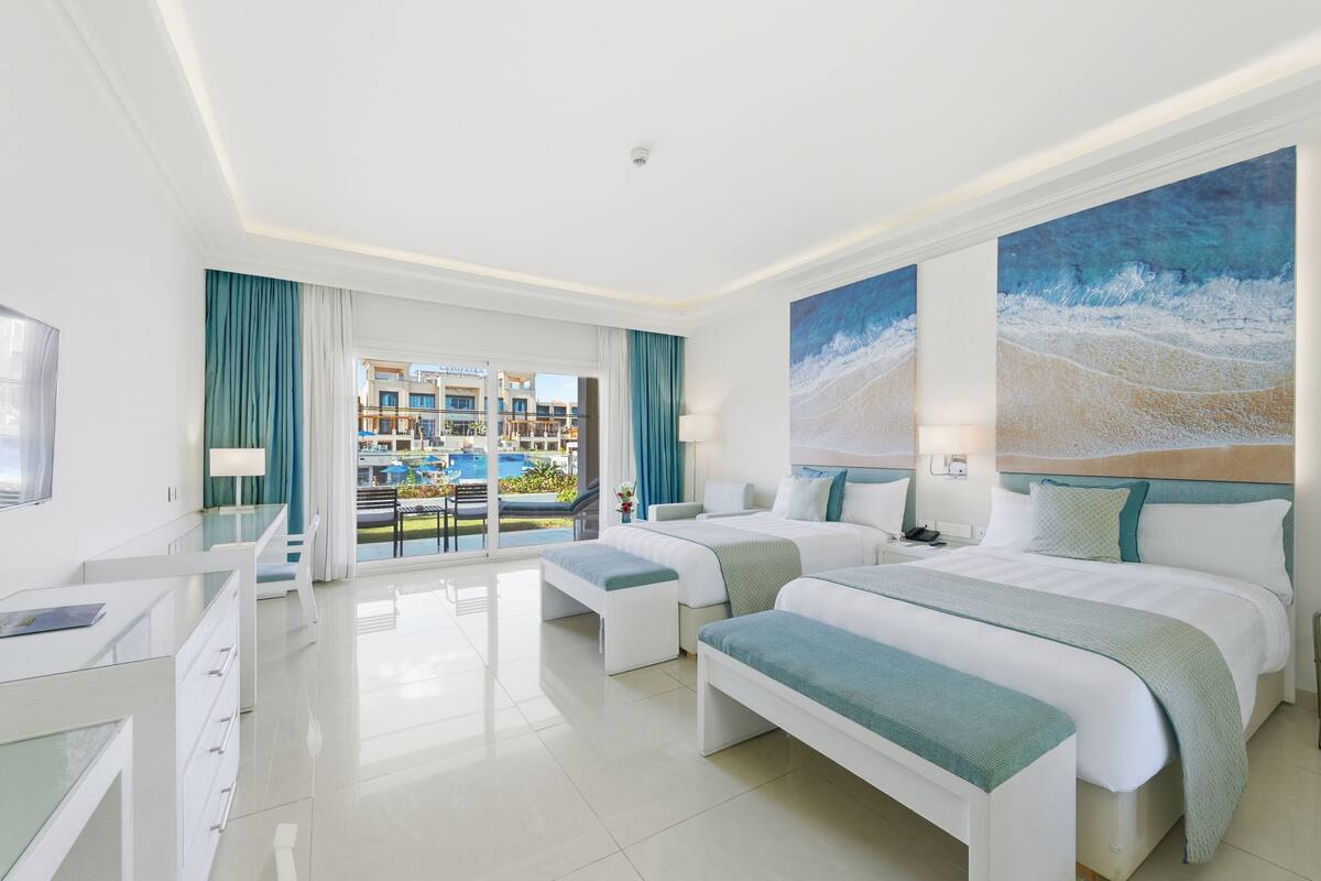 Une chambre d’hôtel moderne avec deux lits, un bureau et une vue sur une piscine et des immeubles.