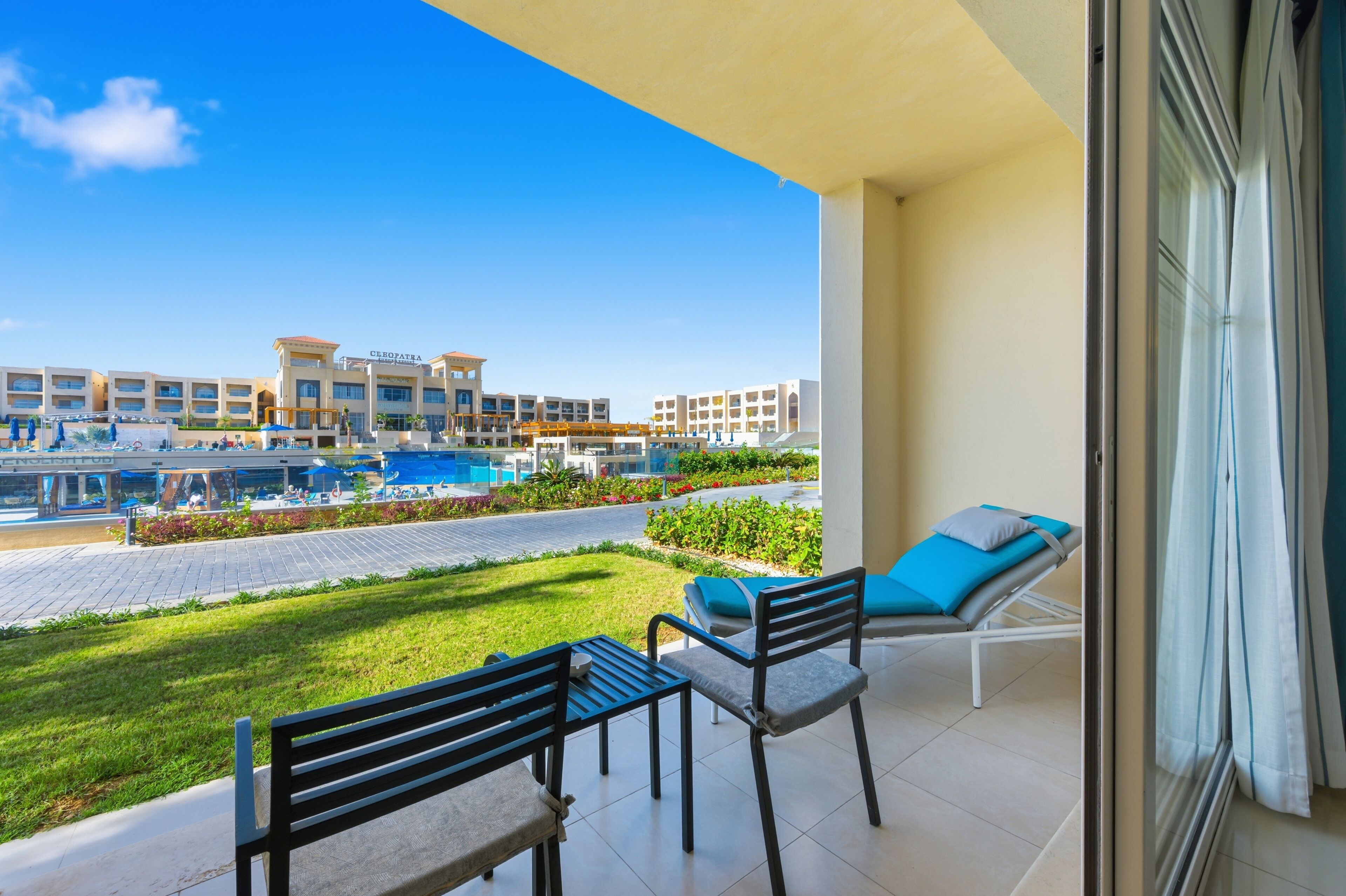 A balcony with a view of a hotel complex, a pool, and a grassy area.