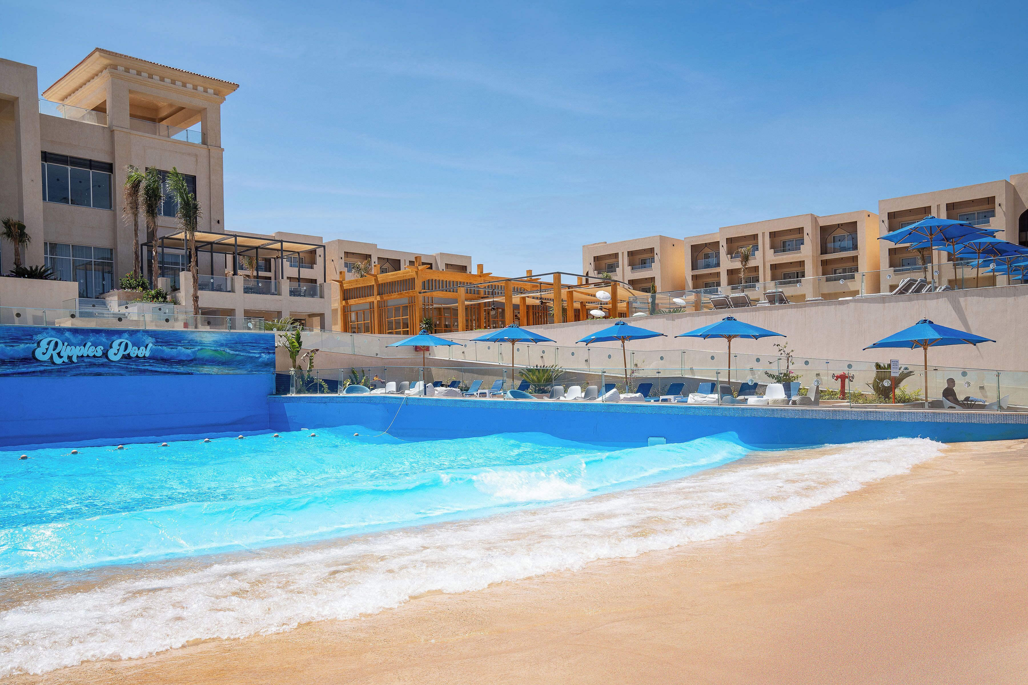 A resort with a swimming pool, beach area, and multiple buildings with balconies.