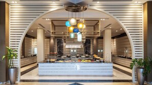 Un hall d’hôtel moderne avec un buffet central, un plafond en arc de cercle et des plantes en pot.