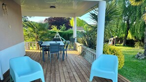 Una terraza de madera con un porche cubierto, una mesa con sillas y dos sillas azul claro.