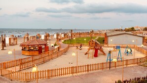 Ein Spielplatz direkt am Strand mit Holzkonstruktionen, einer kleinen Kiosk und einem umzäunten Bereich.
