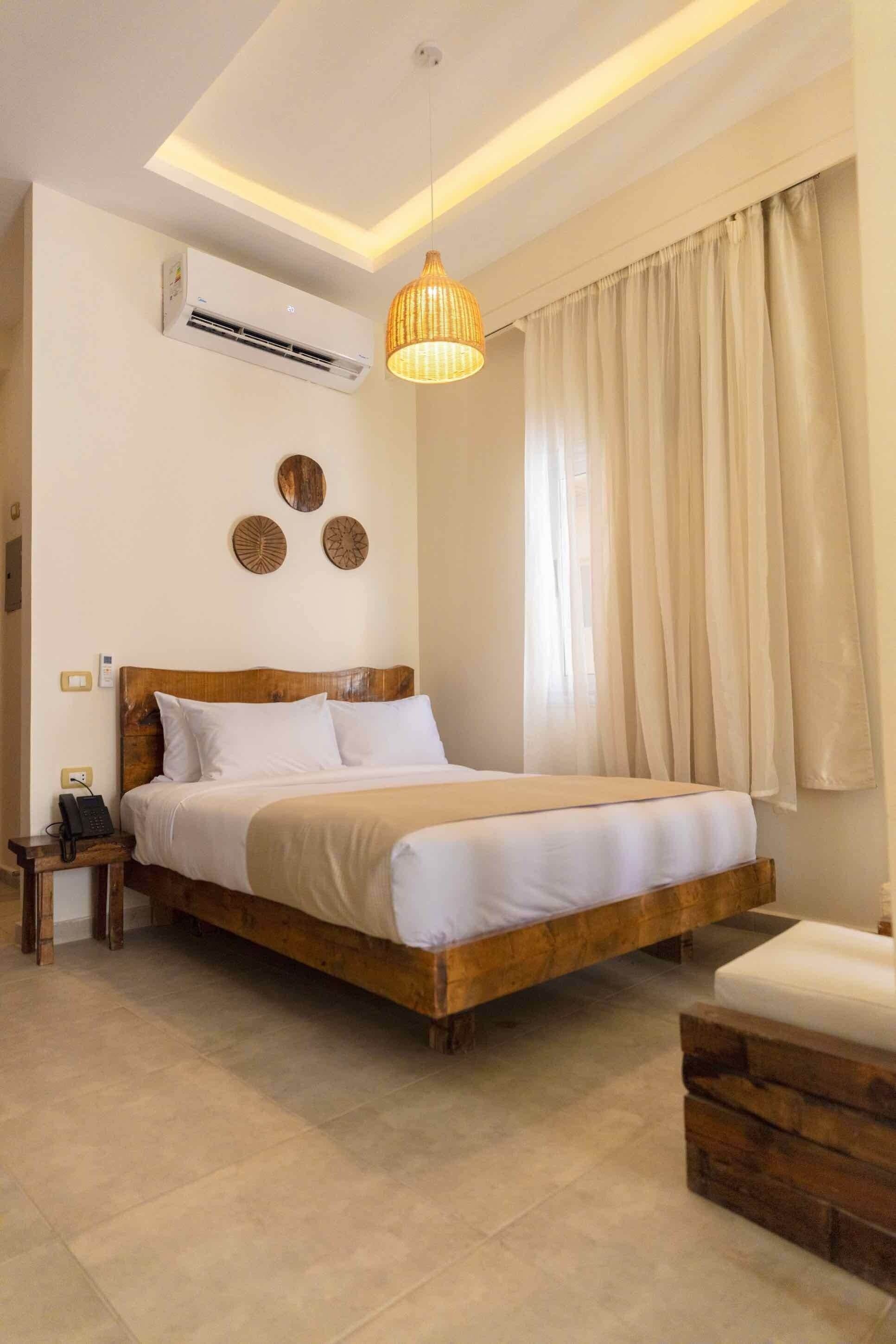 Un dormitorio con cama de madera, mesita de noche con teléfono, aire acondicionado instalado en la pared y lámpara colgante.