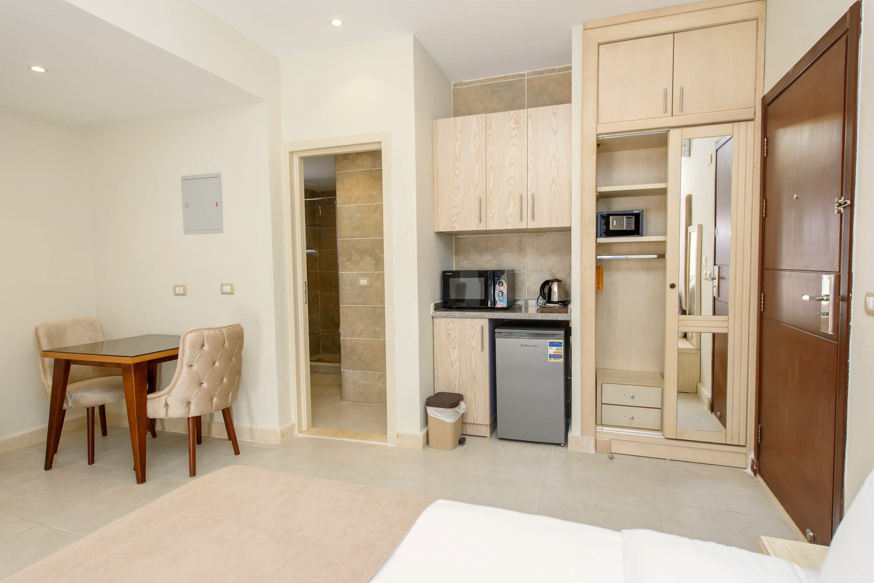 A compact hotel room with a dining area, kitchenette, and wardrobe.