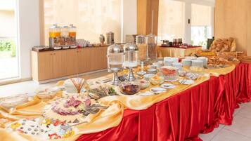 A buffet table with various food items and beverages, set in a bright room with large windows.
