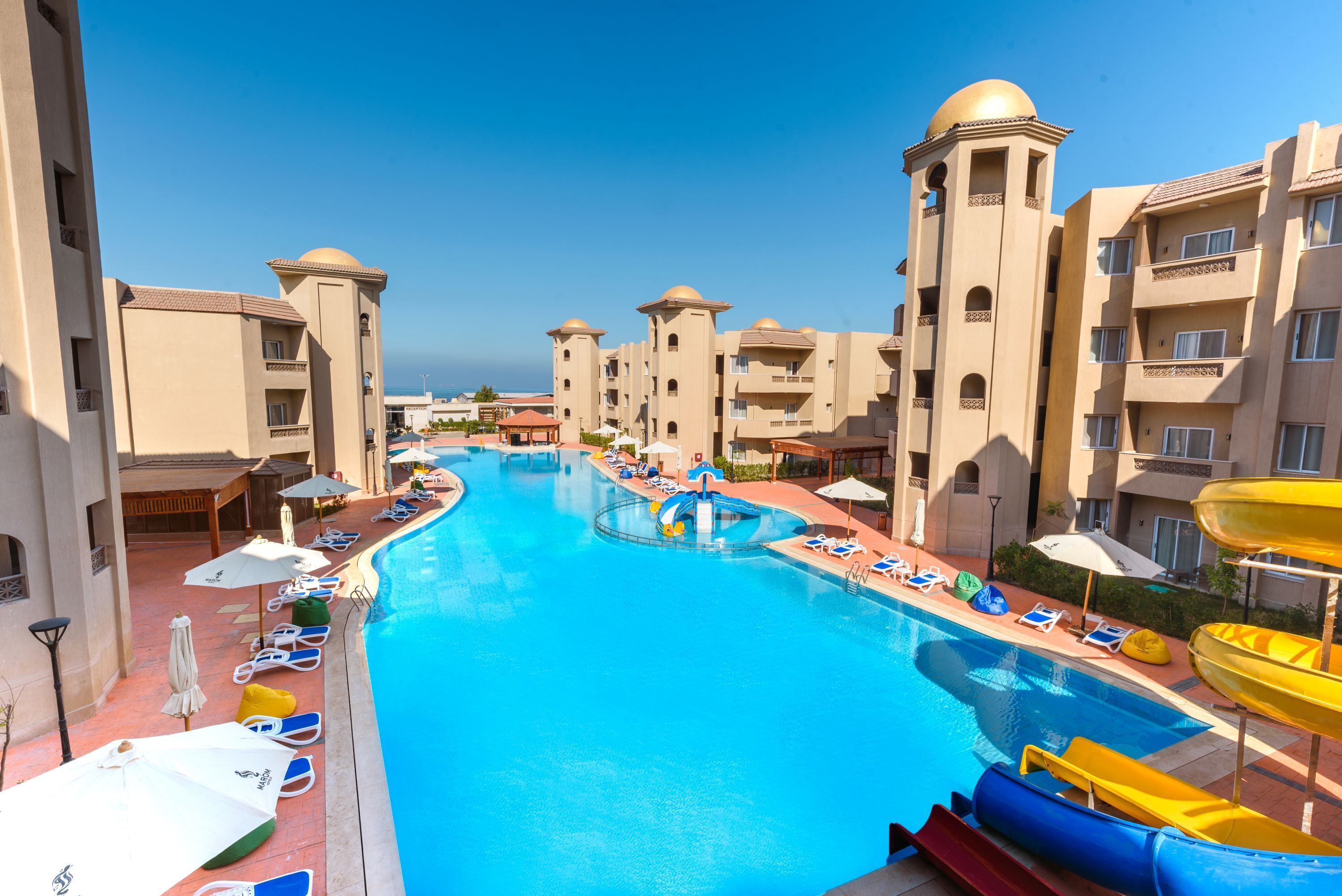 A resort pool area with multiple levels of buildings, a central pool, and a water slide.