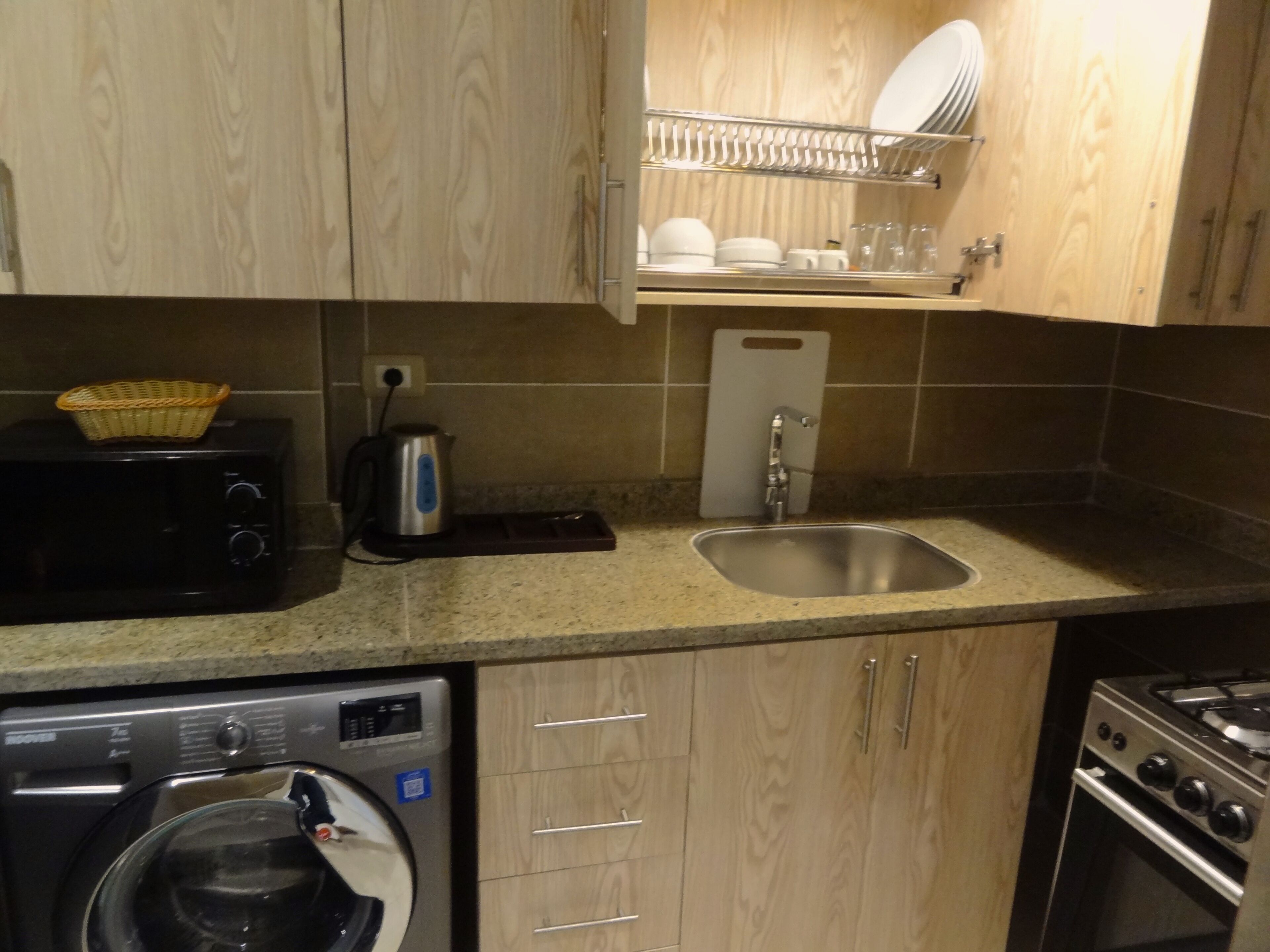 A compact kitchen with a microwave, toaster, sink, and a dish rack.