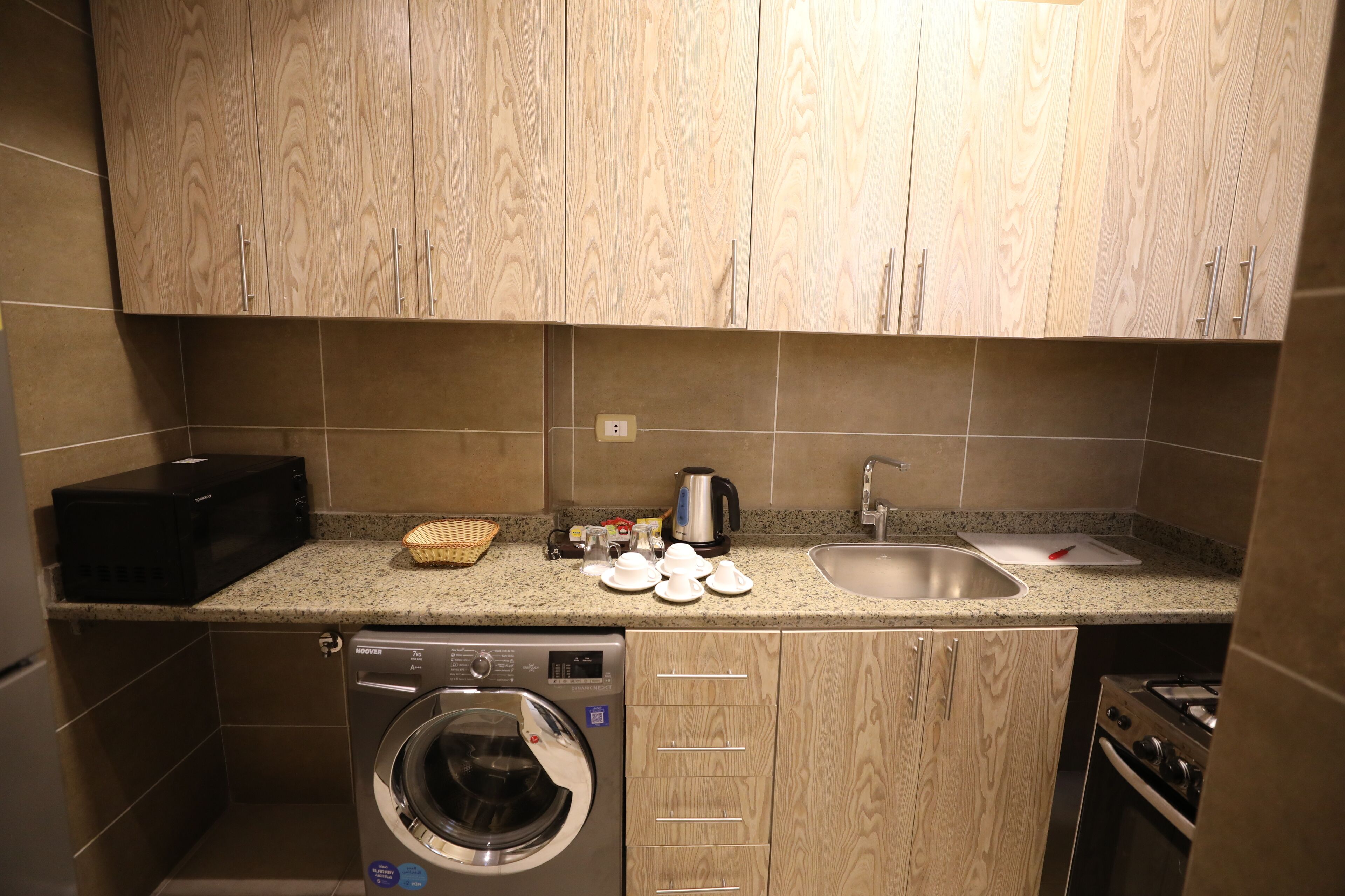 A compact kitchen with wooden cabinets, a washing machine, a microwave, a sink, and a stove.