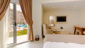 A hotel room with a bed, a desk, a chair, a TV, and a view of a swimming pool and buildings.