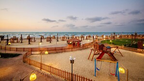 Ein Spielplatz direkt am Strand mit Rutsche, Schaukeln und einer kleinen Laube.